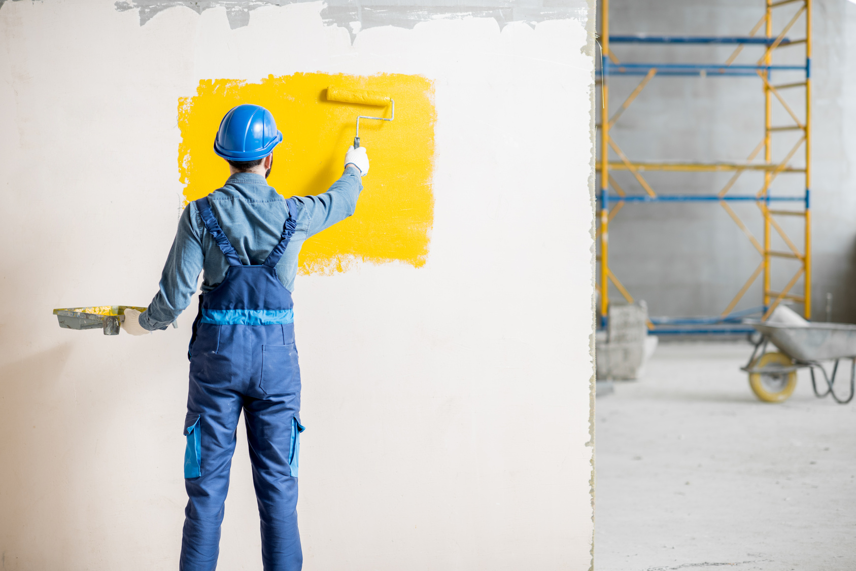 Painter in uniform rolling paint on an interior wall